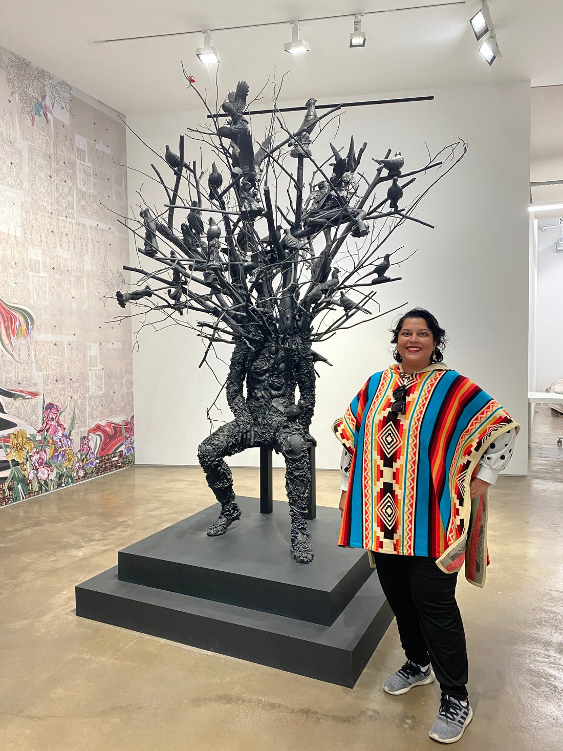 Shree standing next to a Nick Cave sculpture in a brightly colored poncho at the Jack Shainman Gallery in New York City.